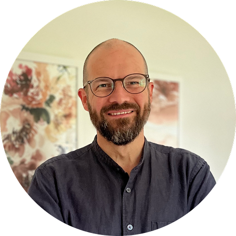 Fred's headshot. He's in his late forties. He's bald, wears glasses, has a beard, and is wearing a blue shirt. He's smiling at the camera.